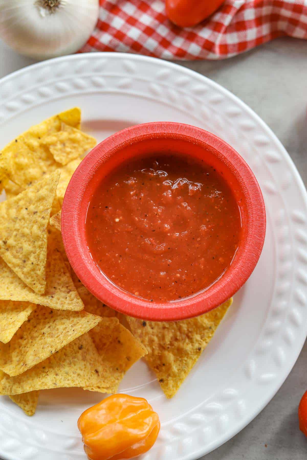 habanero salsa in a red bowl with tortilla chips and tomatoes and peppers around it