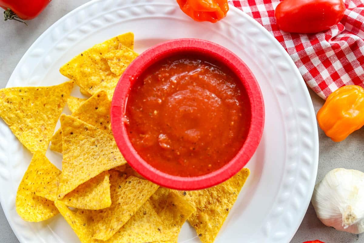 habanero salsa in a red bowl with tortilla chips and tomatoes and peppers around it