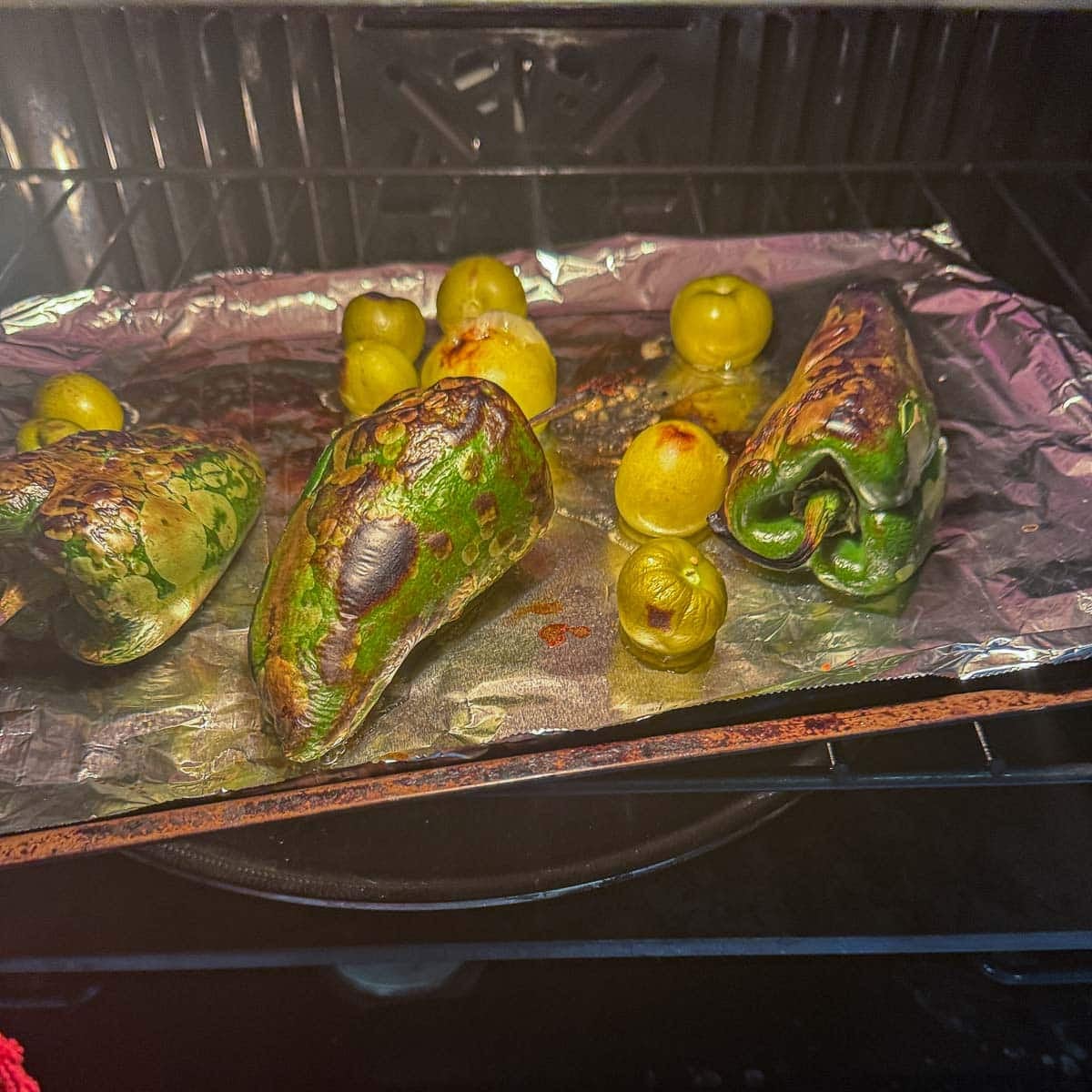 charred poblanos and tomatillos on a foil lined pan for making pork pozole verde