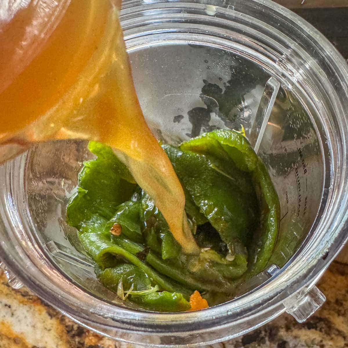 broth being poured over peppers in a plastic blender cup