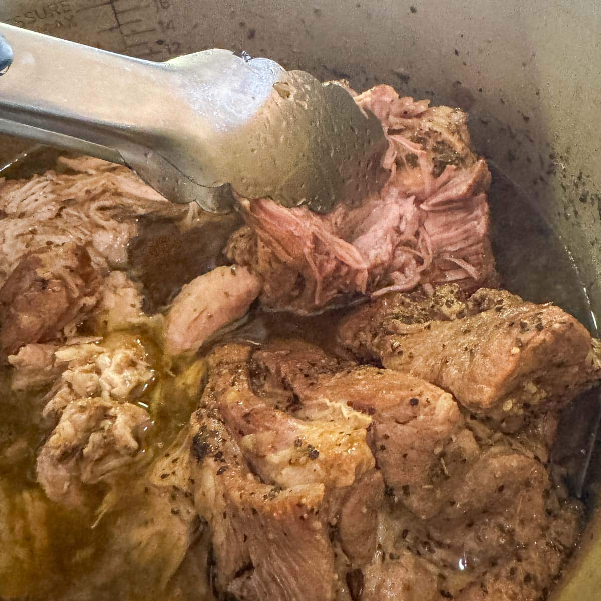 pork being shredded with tongs for pork pozole verde