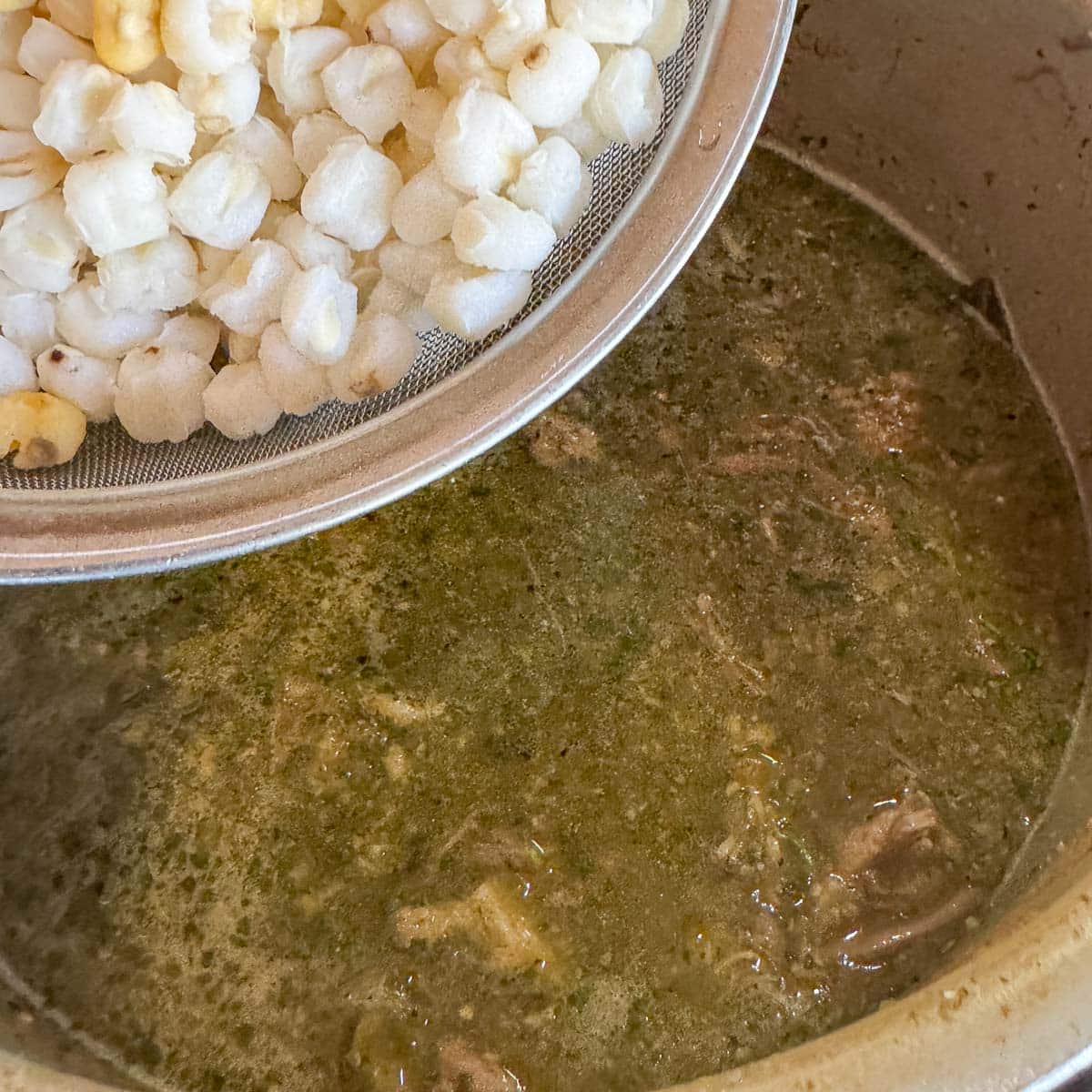 hominy being added to pork pozole verde