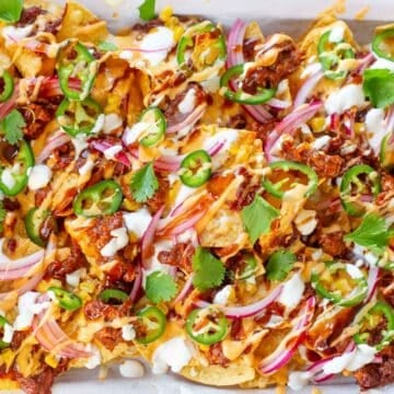 pulled pork nachos recipe in sheet pan topped with fresh cilantro and jalapenos.