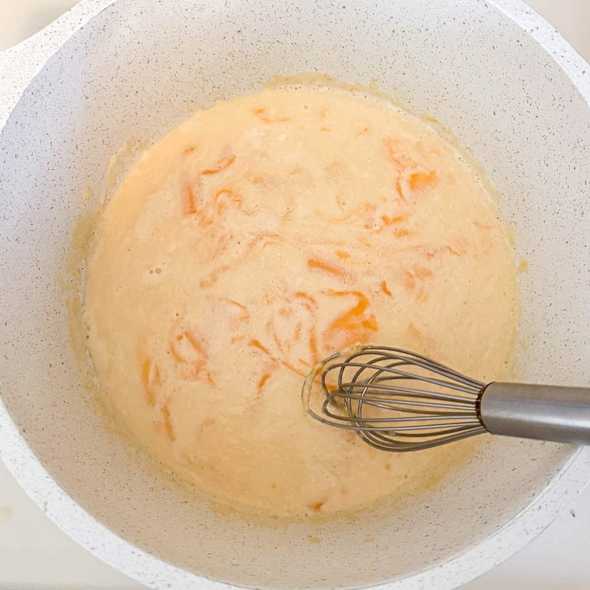 whisking cheese into sauce in pot.