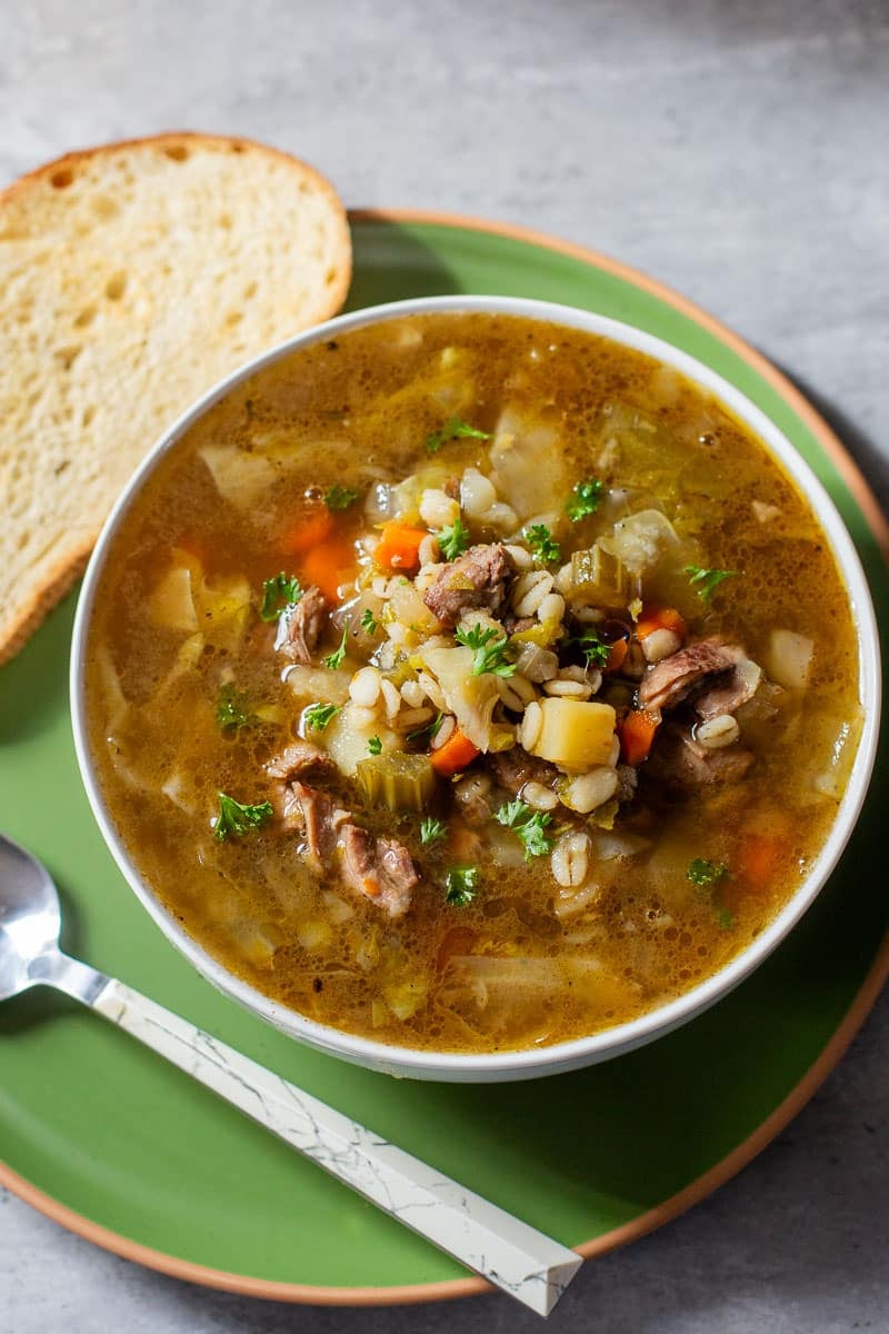 Scotch broth in bowl beside toasted bread and spoon.
