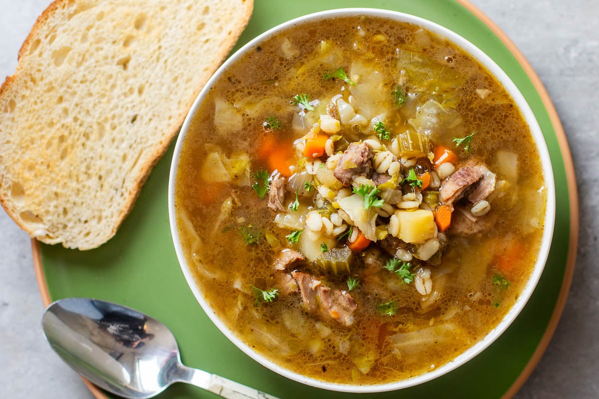 scotch broth recipe in bowl beside bread and spoon.