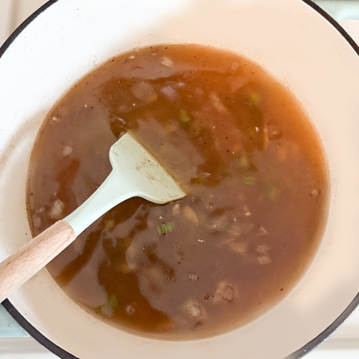 broth added to pot with spatula scraping browned bits from bottom.