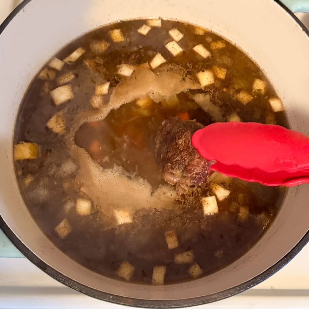 shank being removed from soup with tongs.