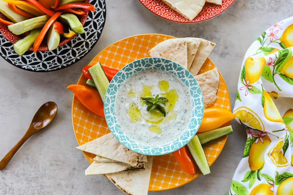 Greek tzatziki sauce with pita bread and fresh veggies served on colorful plates