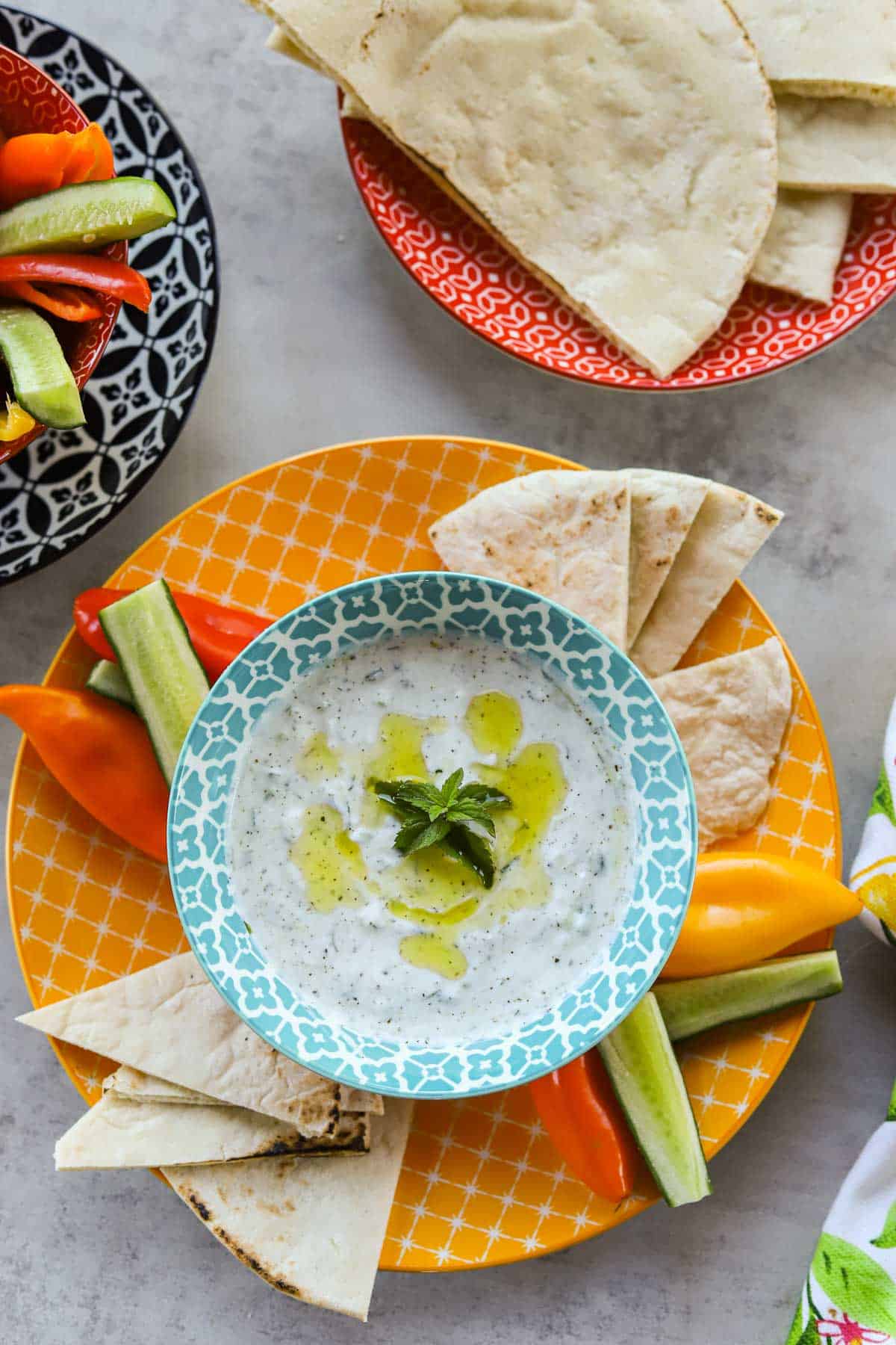tzatziki sauce in a blue and white bowl with pita bread and veggies on colorful plates.