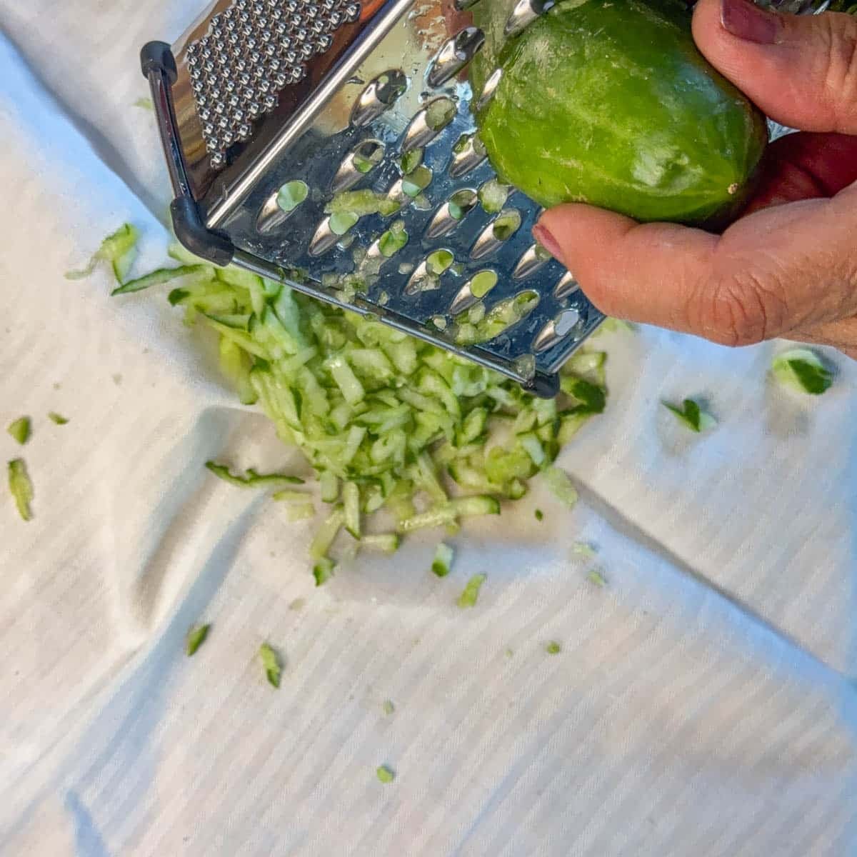 cucumber being grated over a white dish towel