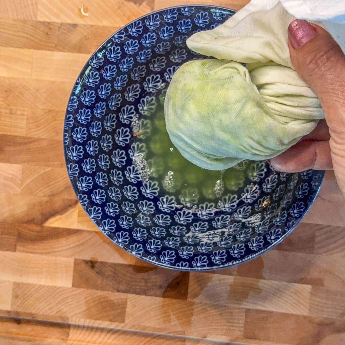 a dishtowel with shredded cucumber being squeezed over a blue bowl.
