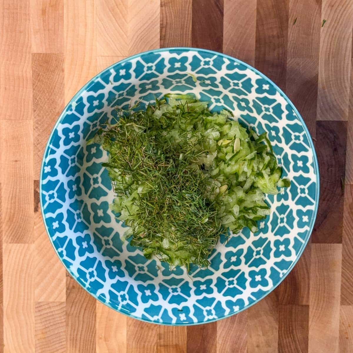 a blue and white bowl with shredded cucumber and fresh chopped dill