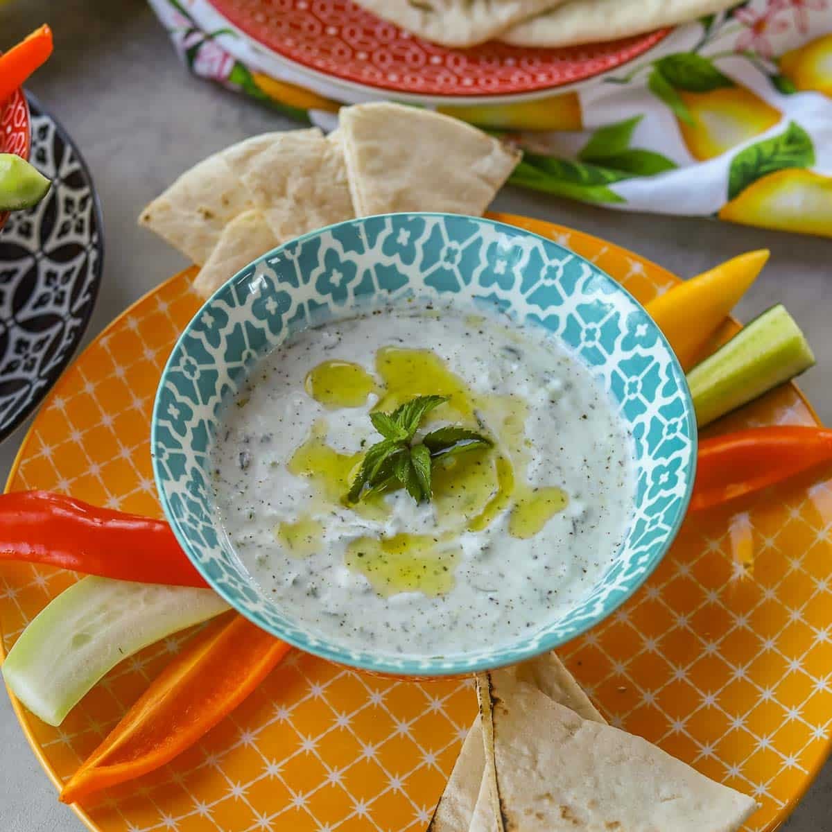 greek tzatziki in a blue and white bowl with veggies and pita wedges
