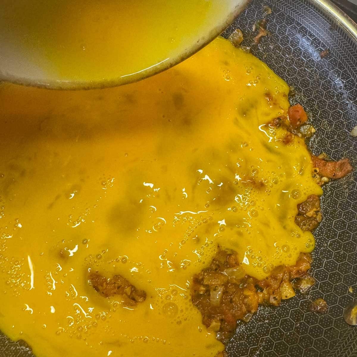 eggs being added to a pan of tomato sauce