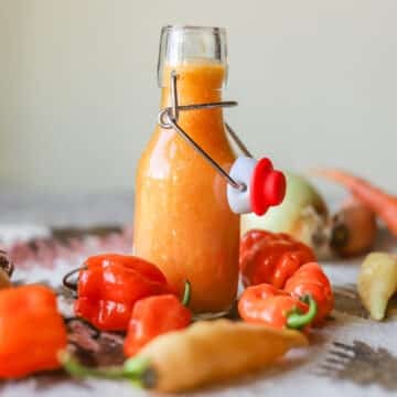 habanero hot sauce in a flip-top bottle with peppers and other veggies around it