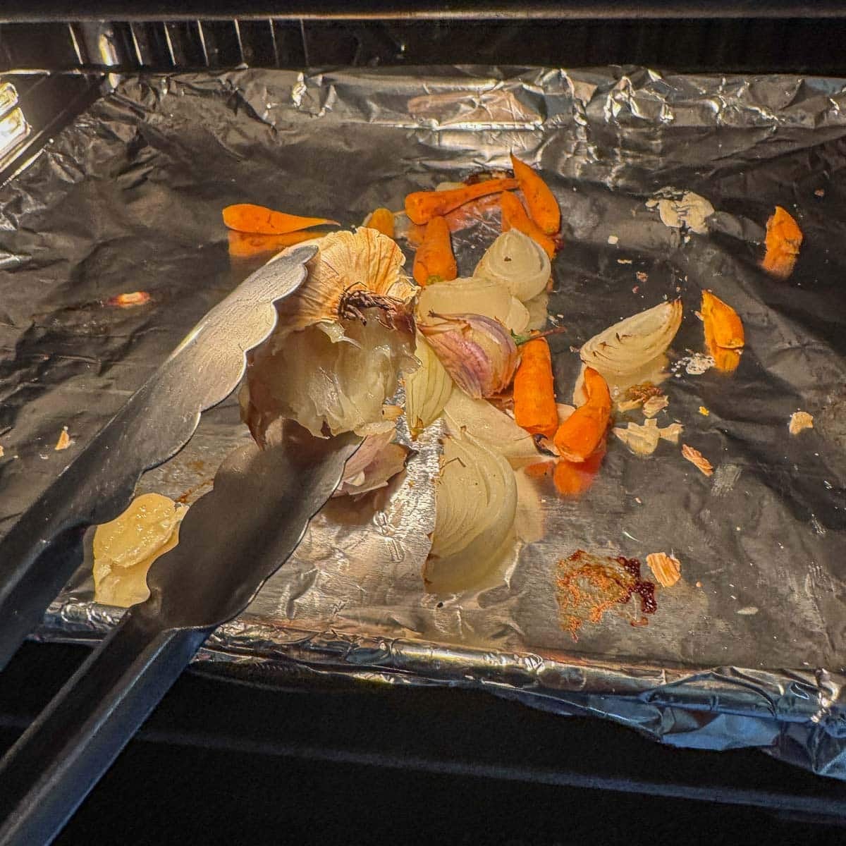 removing roasted garlic with tongs from a tray in the oven