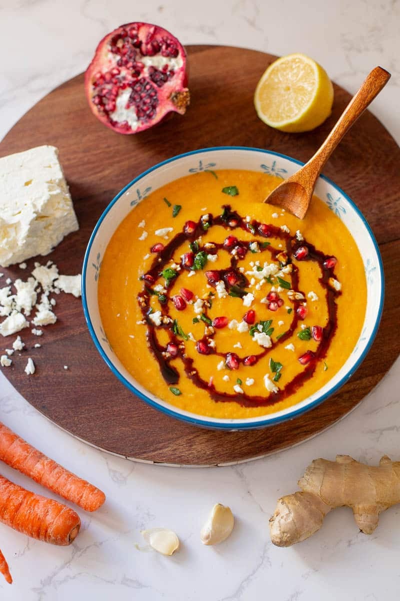 parsnip and carrot soup with a swirl of pomegranate molasses surrounded by carrots, ginger, garlic, lemon, pomegranate, and feta.