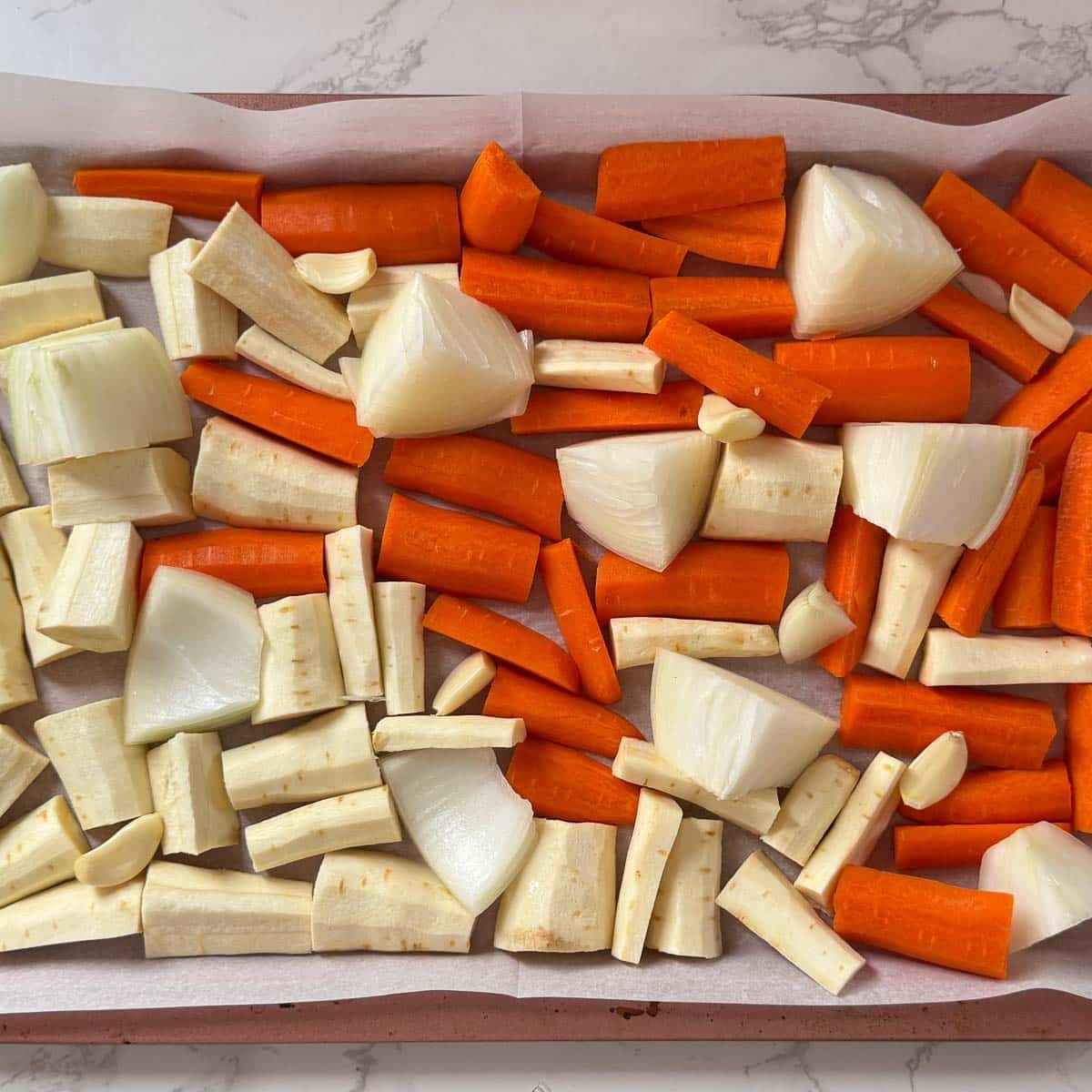 chopped carrot, parsnip, onion, and garlic cloves on baking sheet.