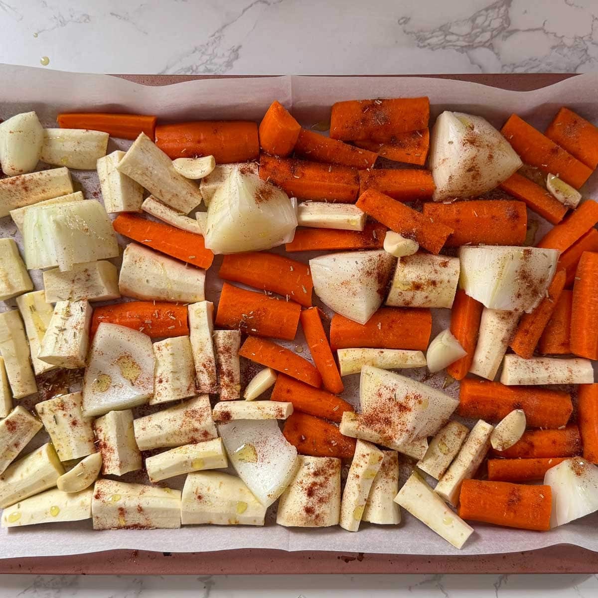 chopped carrot, parsnip, onion, and garlic cloves on baking sheet after seasoning.