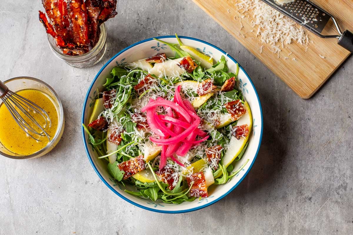 pear rocket salad topped with red onion surrounded by candied bacon, vinaigrette, and parmesan.