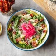 pear rocket salad topped with red onion surrounded by candied bacon, vinaigrette, and parmesan.