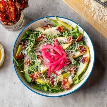 pear rocket salad topped with red onion surrounded by candied bacon, vinaigrette, and parmesan.