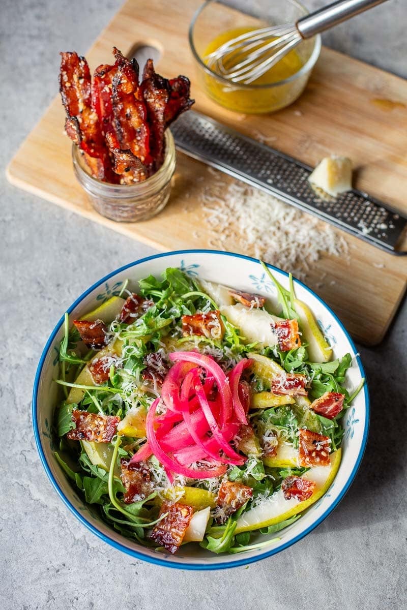 pear rocket salad topped with red onion surrounded by candied bacon, vinaigrette, and parmesan.