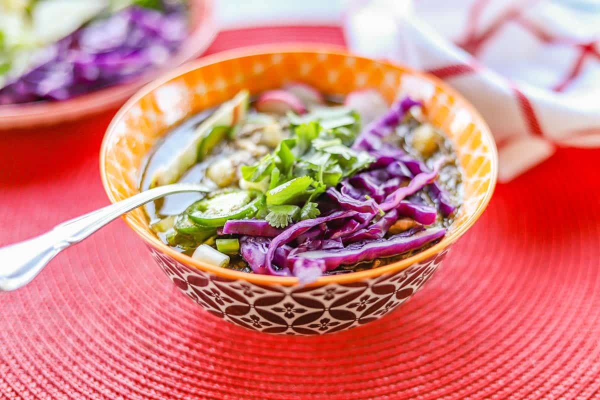 a bowl of pork pozole verde with sliced veggies and herbs.