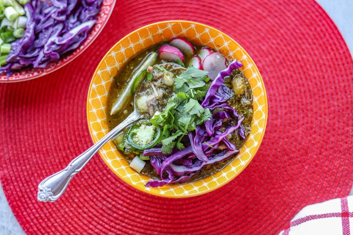 pork pozole verde in a bowl with fresh veggies on a red mat