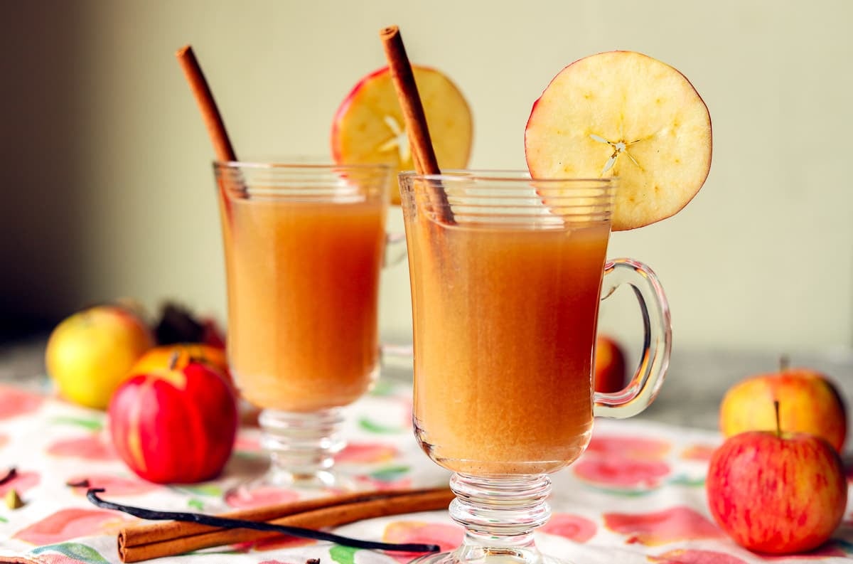 hot apple cider in 2 glasses with cinnamon stick and apple slices