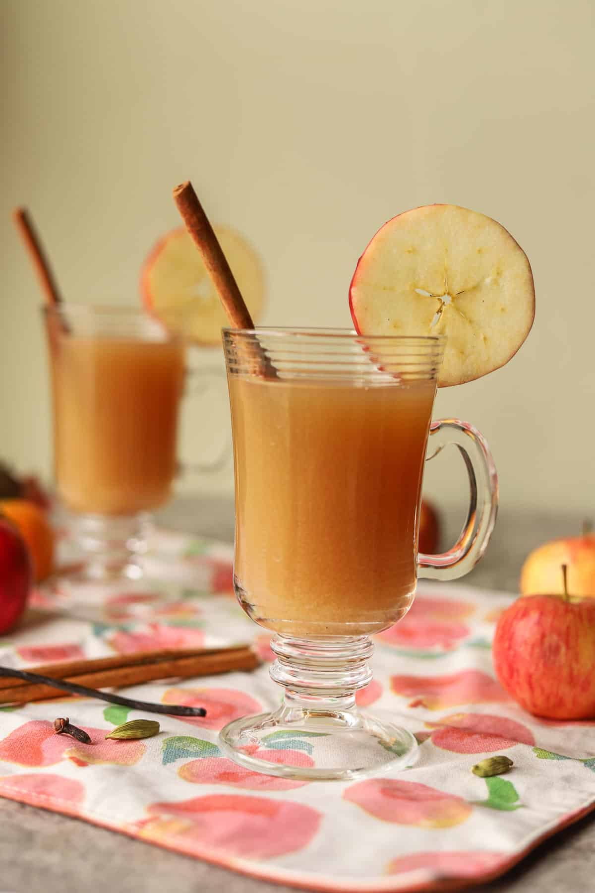 2 glasses of spiced apple cider topped with apple slices and cinnamon sticks