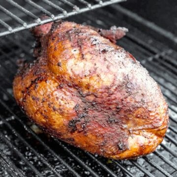 Smoked bone-in turkey breast with golden-brown, seasoned skin on the grates of a pellet grill.